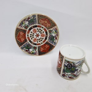 Könnte beinhalten: Eine weiße Porzellan-Teetasse und -Untertasse mit einem farbenfrohen japanisch inspirierten Design. Die Untertasse zeigt ein kreisförmiges Muster aus Blumen, geometrischen Formen und goldenen Akzenten. Die Teetasse hat ein ähnliches Design mit einem floralen Motiv und goldenen Akzenten.