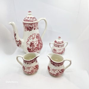 Peut inclure: Un service à thé vintage avec un motif floral rouge et blanc. L'ensemble comprend une théière, un pot à crème, un sucrier et une tasse.