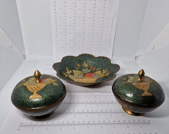 May include: A set of three decorative items: a scalloped-edge dish and two lidded containers. The items are dark green with gold accents and feature a floral design. The containers have a gold finial on top.