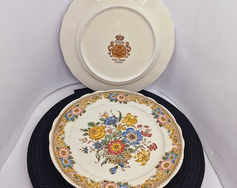 May include: A vintage Royal Staffordshire fine china dinner plate with a floral design. The plate features a bouquet of yellow, red, blue, and white flowers in a basket. The plate has a gold rim and a scalloped edge.