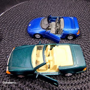 Può includere: Due auto giocattolo decappottabili, una blu e una verde, con le porte aperte e gli interni visibili. L'auto blu è una Lotus e l'auto verde è una Mercedes-Benz.
