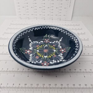K&ouml;nnte beinhalten: Eine kleine, blaue Keramiksch&uuml;ssel mit wei&szlig;em Rand und einem wei&szlig;en Blumenmuster in der Mitte. Das Muster hat rosa, gelbe und gr&uuml;ne Akzente.