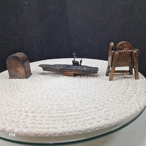 May include: Three miniature bronze sculptures on a white surface. The sculptures include a small chest, a warship, and a grinding wheel. The warship has a detailed design with a tower and antenna. The grinding wheel is supported by a wooden frame.