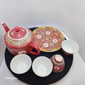 May include: A red and gold Chinese tea set with a teapot, a plate, and four cups. The teapot has a floral design and the words "雙喜" on the side. The plate has a floral design and the words "囍" on the side. The cups are plain white.