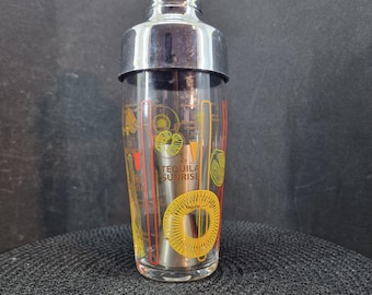 May include: A clear glass cocktail shaker with a stainless steel top and base. The glass is decorated with yellow, orange, and red graphics, including the words "Tequila Sunrise".
