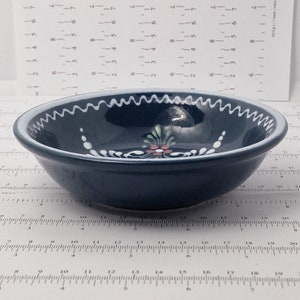 K&ouml;nnte beinhalten: Eine kleine, dunkelblaue Keramiksch&uuml;ssel mit wei&szlig;em Rand und wei&szlig;em Blumenmuster. Die Sch&uuml;ssel hat einen gewellten Rand.