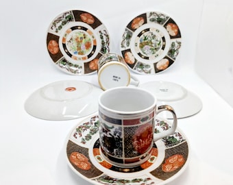 May include: A set of four white porcelain teacups and saucers with intricate black, gold, and red floral designs. The saucers have a wide rim and the cups have a small handle. The cups and saucers are made in China.