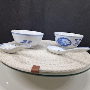 Peut inclure: Deux bols et deux cuillères en céramique blanche avec des motifs floraux bleus. Les bols ont un bord bleu et les cuillères ont un accent bleu. Les bols et les cuillères sont sur un dessous-de-plat rond et tissé.