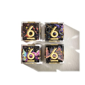Op de afbeelding: Vier vierkante compacts met een gouden nummer 6 op een zwarte achtergrond met kleurrijke accenten. De compacts zitten in doorzichtige hoesjes met gouden randen. De achtergrond heeft een galaxiethema met sterren en kleurrijke nevelachtige ontwerpen.