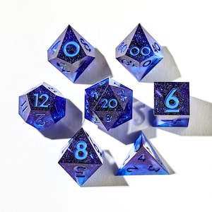 May include: Set of seven blue and white galaxy dice with black numbers. The dice are a d4, d6, d8, d10, d%, d12, and d20.