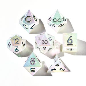 May include: Set of seven iridescent white dice with black numbers. The dice are a d4, d6, d8, d10, d%, d12, and d20.