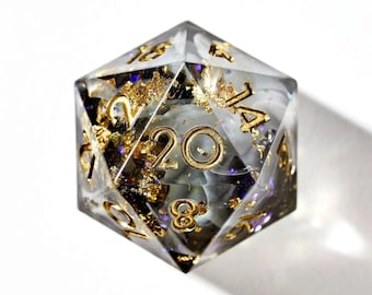 May include: A clear, iridescent, 20-sided die with gold numbers and flecks of gold leaf. The die is a popular tool for tabletop role-playing games.