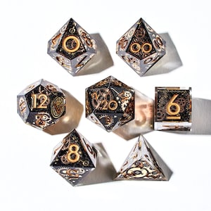 May include: Set of seven black and gold dice with intricate gear designs. The dice are numbered 4, 6, 8, 10, 12, and 20.