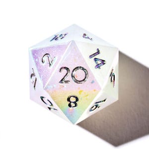 May include: A white iridescent 20-sided die with black numbers. The die is showing the number 20.