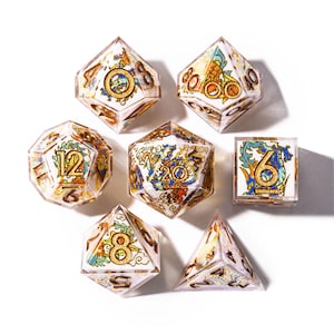May include: Set of seven clear, multi-sided dice with ornate gold, blue, and orange designs. Each die features a different number and decorative elements. The dice are arranged on a white surface.