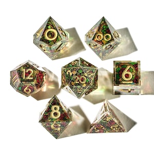 Peut inclure: Ensemble de sept dés polyédriques avec un motif de vitrail. Les dés présentent des chiffres dorés et des motifs floraux colorés dans des tons de rouge, vert et jaune. Les dés sont conçus pour les jeux de société.