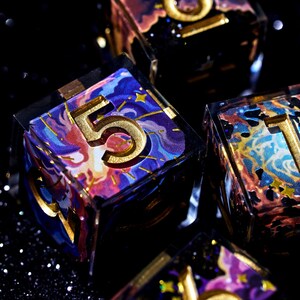 May include: Close-up of several dice with a celestial theme. The dice are clear with colorful, swirling designs in shades of blue, purple, and gold. Each die has a large, gold number on its face, with a glittery black background.