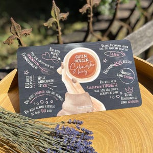 Könnte beinhalten: Eine rechteckige schwarze Karte mit einer zentralen Illustration von Händen, die eine Kaffeetasse mit dem Text Guten Morgen Schwesterherz halten. Die Karte ist mit verschiedenen handgeschriebenen deutschen Sprüchen, Sternen, Herzen und einer Feder verziert.