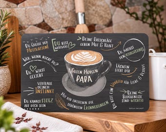 May include: A rectangular dark gray placemat featuring a central illustration of a coffee cup with latte art and the text "Guten Morgen PAPA". The surface is decorated with various German phrases, a heart, and a feather graphic in white and gold.