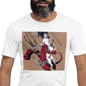 May include: White t-shirt with a graphic print of a red demon with a woman riding on its back. The demon has horns and a tail. The woman is wearing a white dress and has long black hair. The background is brown with a pattern of arrows.