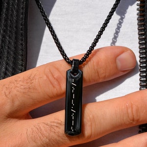 May include: A black leather jacket with a zip fastening and a black chain necklace with a rectangular pendant. The pendant has white dots arranged in a pattern.