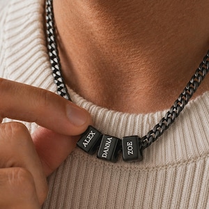 May include: A black chain necklace with three personalized name beads. The beads are engraved with the names "ALEX", "DANNA", and "ZOE" in white lettering. The necklace is a dark gunmetal color.