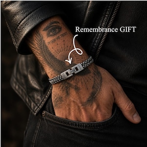 Könnte beinhalten: Ein silberfarbenes Armband aus geflochtener Metallkette mit einem rechteckigen Verschluss, der mit dem Jahr 2020 und dem Wort LOVED graviert ist. Der Text Remembrance GIFT ist mit einem Pfeil zum Verschluss sichtbar.