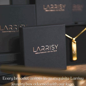 Może przedstawiać: Czarne pudełko na biżuterię z napisem "LARRISY Make a Statement. Own Your Style." w złotych literach. Pudełko jest otwarte, a wewnątrz widać złoty naszyjnik z zawieszką.