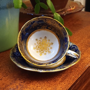 May include: A blue and gold teacup and saucer set with a floral design. The cup and saucer are both decorated with a gold trim and a floral pattern in the center.
