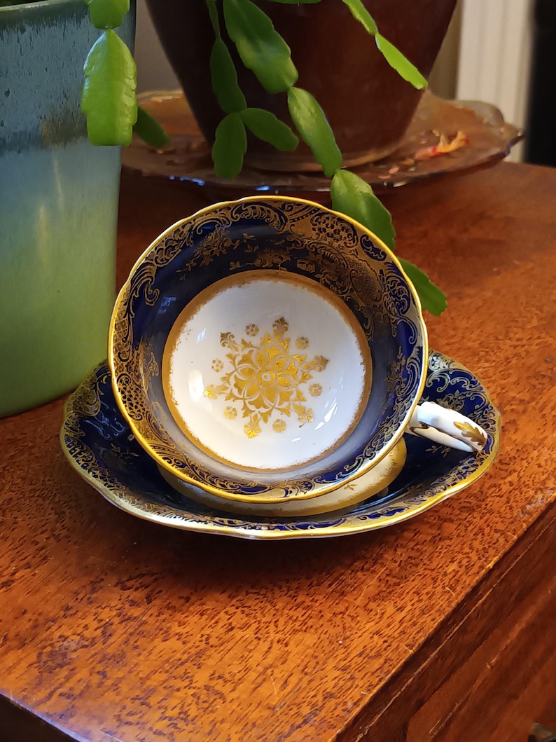 May include: A blue and gold teacup and saucer set with a floral design. The cup and saucer are both decorated with a gold trim and a floral pattern in the center.