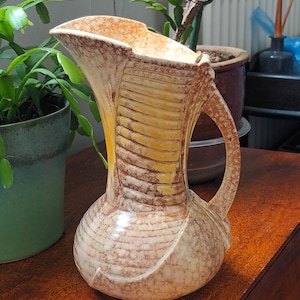 Peut inclure: Un pichet en céramique avec un glaçage jaune et brun. Le pichet a une large ouverture et une anse. Il a une surface texturée et un design unique.