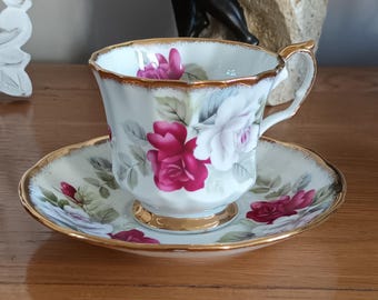 May include: A white teacup and saucer with a gold rim. The teacup and saucer are decorated with a floral pattern of pink and white roses.