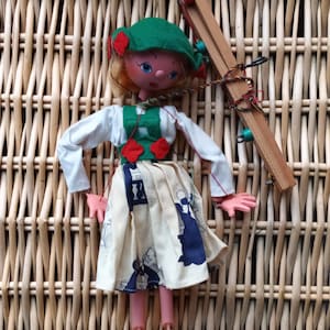 Puede incluir: Muñeca marioneta vintage con sombrero verde, blusa blanca y falda crema con estampados azules y blancos. La muñeca tiene pelo rubio, manos y piernas rosas y pies de madera. Se adjunta un control de madera.
