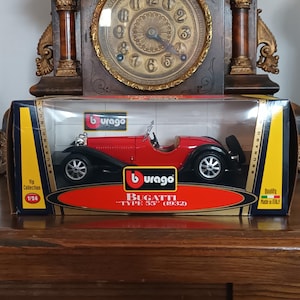 Op de afbeelding: Een rood en zwart Bugatti "Type 55" (1932) modelauto in een transparante displaydoos. Het model is schaal 1/24. De doos heeft het Burago-logo en tekst. De auto heeft zilveren wielen.