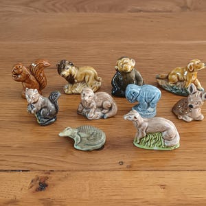 以下が含まれることがあります： リス、ライオン、サル、犬、ゾウ、シカ、ワニなど、小さなセラミック製の動物フィギュアのコレクション。 フィギュアは様々な色で塗装されており、木製の表面に置かれています。