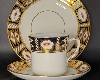 May include: A white teacup and saucer set with a blue and gold floral pattern. The cup has a gold rim and the saucer has a gold band around the edge.