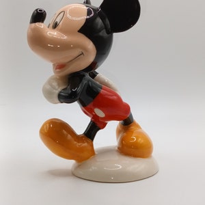 May include: A ceramic figurine of Mickey Mouse, standing with his right leg forward and his left arm bent. He is wearing red shorts with a white dot, black shoes, and a black and white face.