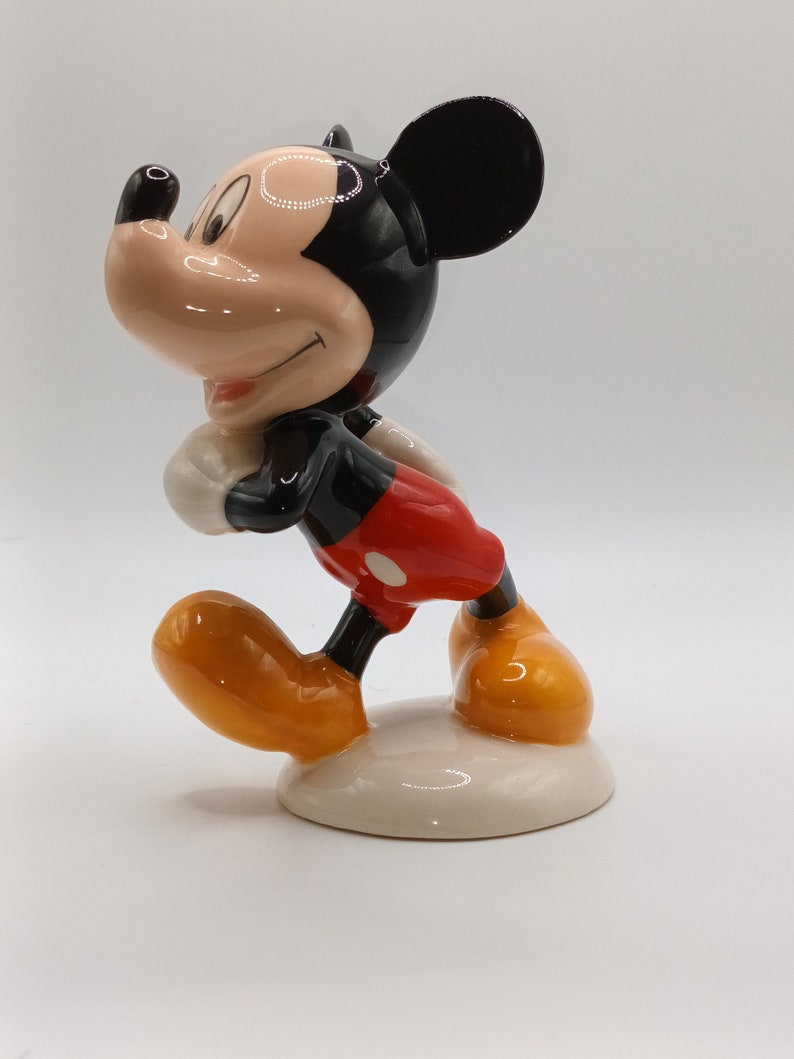 May include: A ceramic figurine of Mickey Mouse, standing with his right leg forward and his left arm bent. He is wearing red shorts with a white dot, black shoes, and a black and white face.