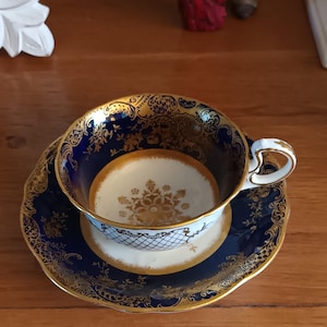 May include: A blue and gold teacup and saucer set with a floral design. The cup has a heart-shaped handle.