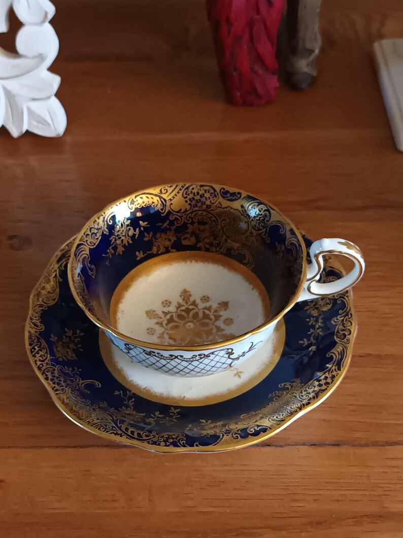 May include: A blue and gold teacup and saucer set with a floral design. The cup has a heart-shaped handle.