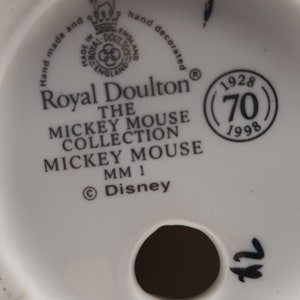 May include: White ceramic figurine base with a Royal Doulton logo, the text "The Mickey Mouse Collection Mickey Mouse MM 1", and a copyright symbol with "Disney". The base also has a circular mark with the text "1928 (70) 1998".