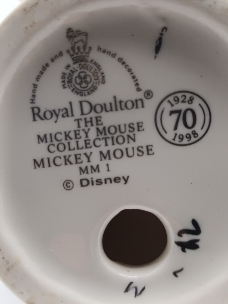 May include: White ceramic figurine base with a Royal Doulton logo, the text "The Mickey Mouse Collection Mickey Mouse MM 1", and a copyright symbol with "Disney". The base also has a circular mark with the text "1928 (70) 1998".