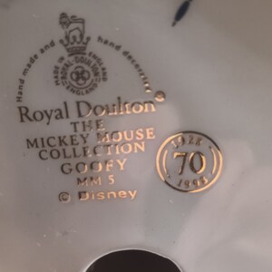 May include: A gold Royal Doulton figurine of Goofy from the Mickey Mouse Collection. The figurine is marked with the year 1996 and the number 70. The text "Hand made and hand decorated" is visible on the base.