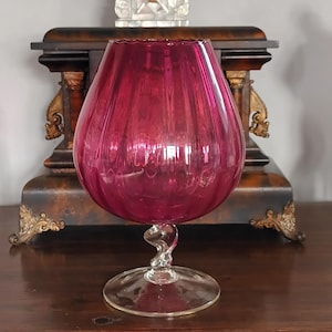 Puede incluir: Una taza de cerámica blanca con un asa negra y el texto "But First, Coffee" en un estilo manuscrito. La taza está sobre una superficie blanca. La taza mide aproximadamente 10 cm de alto.