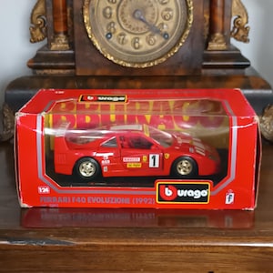 May include: A red Ferrari F40 Evoluzione (1992) model car in a red box. The model is 1:24 scale and features the number 1. The box has the "burago" logo.