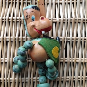 Puede incluir: Marioneta de hipopótamo Pelham Puppets vintage. La marioneta tiene una cara pintada con ojos azules, boca roja y una capa de fieltro verde con un parche amarillo. Su cuerpo es de color canela claro y sus extremidades son de cuentas de madera verdes.