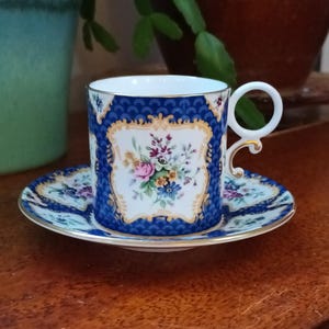 May include: A blue and white porcelain teacup and saucer set with a floral design. The cup has a gold rim and a handle. The saucer has a gold rim and a floral design.