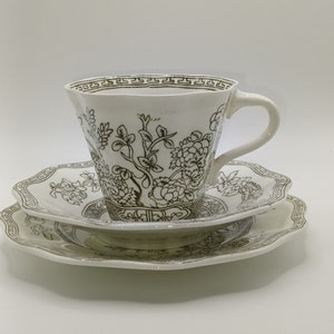 Könnte beinhalten: Ein weißes Tee-Set mit schwarzem und goldenem Blumenmuster. Die Tasse hat einen gewellten Rand und einen Henkel. Die Untertasse hat einen gewellten Rand.