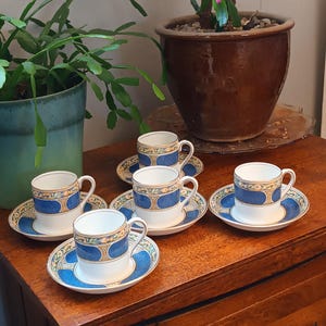 Könnte beinhalten: Satz mit fünf blauen und goldenen Teetassen und Untertassen mit floralem Muster. Die Tassen und Untertassen sind auf einem Holztisch angeordnet.