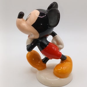 May include: A ceramic figurine of Mickey Mouse in a walking pose. He is wearing his signature red shorts, yellow shoes, and black ears. The figurine is painted in bright colours and has a glossy finish.